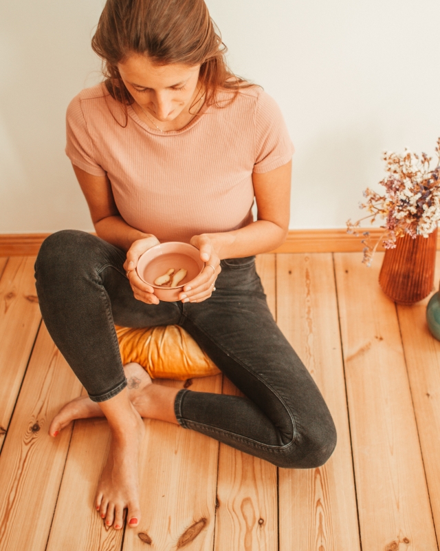 Ayurveda Expertin Jenny Lehnen sitzt auf einem Yogakissen und hält einen Ingwertee in der Hand.